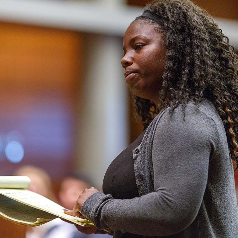 Black woman holding notepad in front of audience at event.